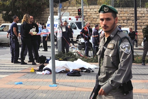 photo - A border policeman walks past the covered body of a victim of the terror attack near the Jerusalem light rail in November 2014