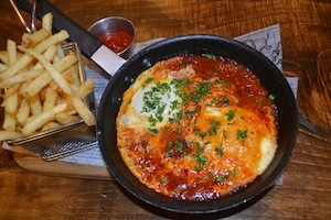 photo - My shakshuka ($14.50) arrived on a skillet, presented on a wooden board accompanied by French fries in a neat stainless steel basket.