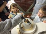 Ben Harrington churns the wheat while Joel Harrington and Sara Basya Mochkin look on