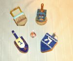 photo - Dreidels from the author’s dreidel collection. Clockwise from the top left: a hand-painted dreidel with an open top; a hand-painted dreidel on a base; a felt dreidel; a hand-painted dreidel; and, in the centre, a tiny hand-painted glass dreidel
