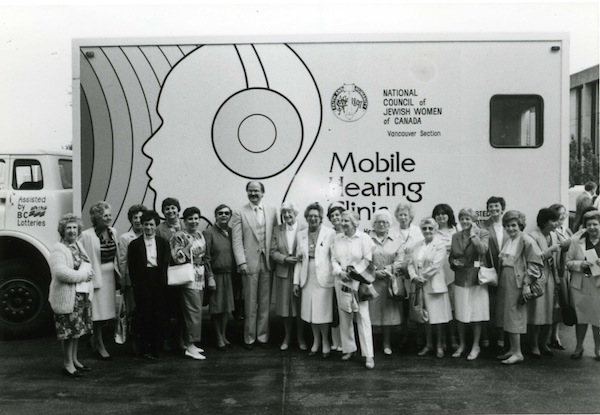photo - Then-Vancouver mayor Mike Harcourt and members of National Council of Jewish Women in front of the first Mobile Hearing Clinic, outside Vancouver City Hall on June 11, 1984. After raising the funds to build and operate the clinic on a trial basis, NCJW sold it to the provincial health department for the nominal price of $1. They did the same with a second mobile clinic in 1986
