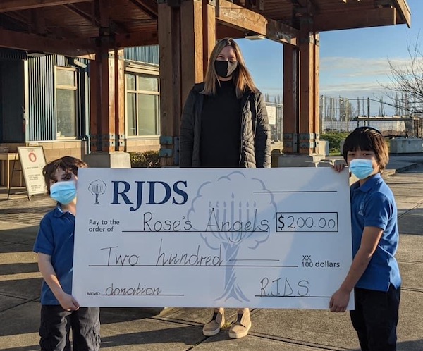 photo - Outside Richmond Jewish Day School, Courtney Cohen accepts a donation to Rose’s Angels, which was collected by RJDS students and staff