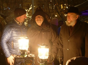 photo - Left to right: Ezra Shanken, Arnold Silber and Rabbi Yitzchak Wineberg try to keep warm at the lighting of the Silber Family Agam Menorah Dec. 18