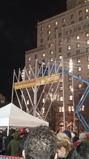 photo - The first candle on the Silber Family Agam Menorah was lit by Etsik Mizrachi and Dan Mizrachi, father and brother, respectively, of Ben Mizrachi, z”l
