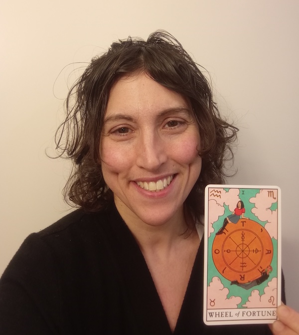 photo - Alycia Fridkin holds the Wheel of Fortune tarot card, which features the Tetragrammaton of G-d’s name interspersed between the letters T, A, R, O